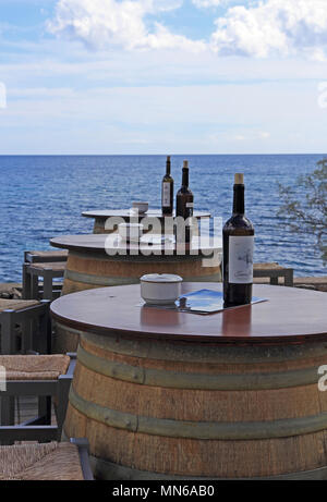 Barrels support table top with ashtrays and wine bottles outside seafront bar, Cala Bona, Mallorca Stock Photo