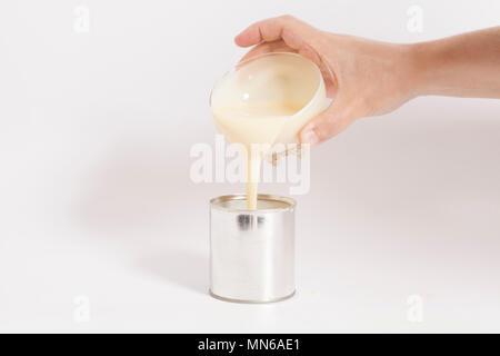 Man hand pouring condensed milk into a tin can over white background Stock Photo