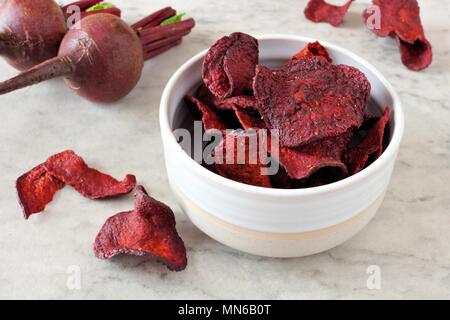 Bowl of healthy beet chips over a white marble background Stock Photo