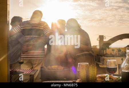 Group of four caucasian friends mature over 70 retired celebrate love and friendship in front of a golden sunset from a terrace rooftop. dinner on the Stock Photo