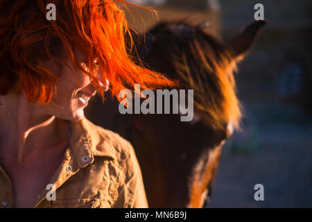 red hair beautiful young woman lifestyle with best friend horse in countryside. portrait of paople and animals for pet life concept outdoor under the  Stock Photo