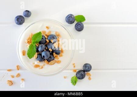 Greek yogurt with blueberries and granola, above view on white wood Stock Photo