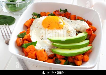 Breakfast nutrient bowl with sweet potato, egg, avocado and spinach, close up table scene Stock Photo
