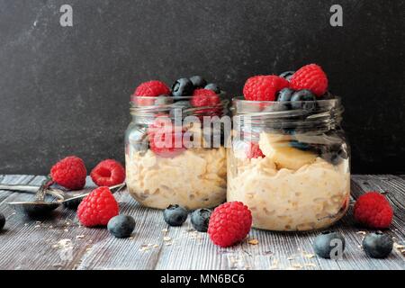 Overnight oats with fresh blueberries and raspberries in jars on a rustic dark background Stock Photo