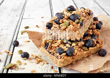 Two stacked superfood breakfast bars with oats and blueberries, side view on rustic white wood Stock Photo