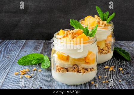 Tropical mango and pineapple parfaits in mason jars, scene on dark rustic background Stock Photo