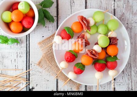 Plate of delicious summer fruit skewers with melon, cheese and prosciutto on a rustic white wood background Stock Photo