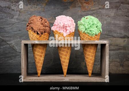 Chocolate, cherry and pistachio ice cream in waffle cones in rustic wood holder over a slate background