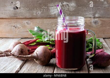Fresh beet juice in a mason jar glass with beets over a rustic wood background Stock Photo