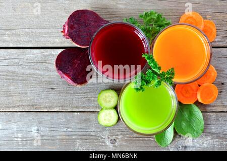 Three glasses of healthy vegetable juice with surrounding ingredients, above view over rustic wood Stock Photo