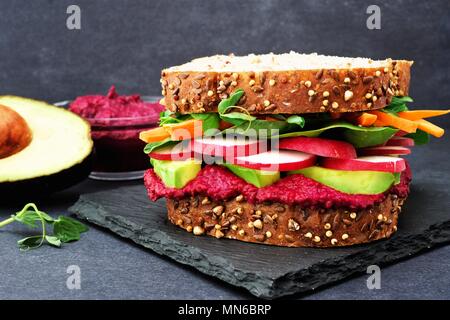 Superfood sandwich with beet hummus, avocado, vegetables and greens, on whole grain bread against a slate background Stock Photo