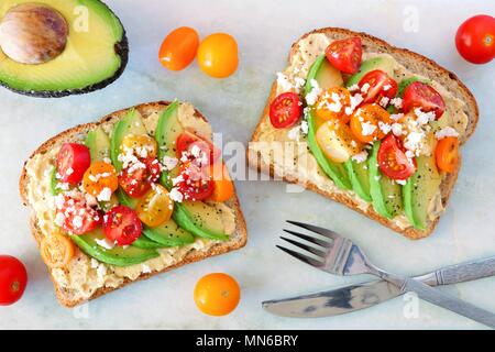 Avocado toasts with hummus and tomatoes, overhead view on white marble background Stock Photo