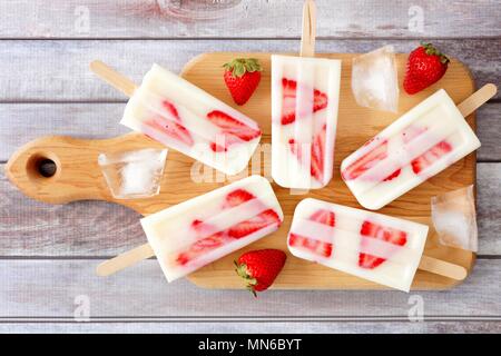 Homemade strawberry vanilla popsicles on a paddle board with a rustic wood background Stock Photo