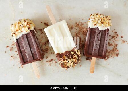 Chocolate and almond dipped white and dark popsicles, overhead view over a marble background Stock Photo