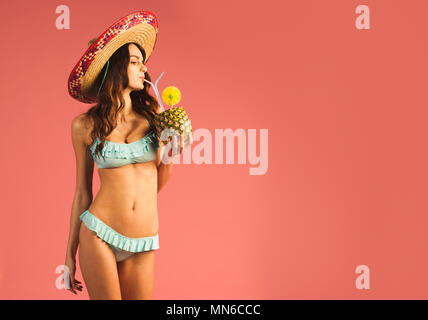 young beautiful woman in bikini and sombrero drinking exotic tropic cocktail isolated on pink background Stock Photo