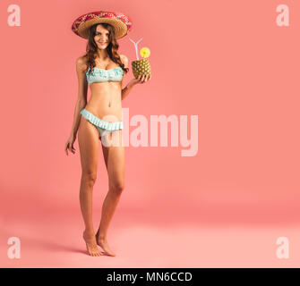 young beautiful woman in bikini and sombrero with exotic tropic cocktail isolated on pink background Stock Photo