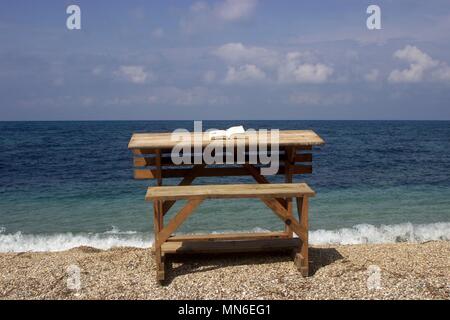 Wooden desk on a beach with an open book on it and blue sea as a background Stock Photo