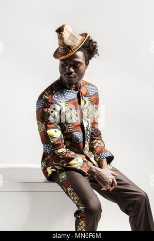 African man in national kongo costume sit on coub . Indoor, isolated on gray background Stock Photo