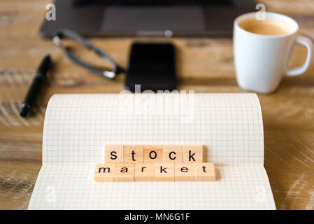 Closeup on notebook over wood table background, focus on wooden blocks with letters making Stock Market words. Business concept image. Laptop, glasses Stock Photo