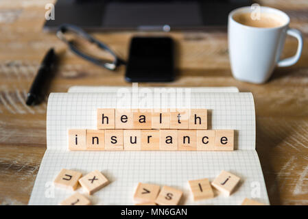 Closeup on notebook over wood table background, focus on wooden blocks with letters making Health Insurance words. Stock Photo