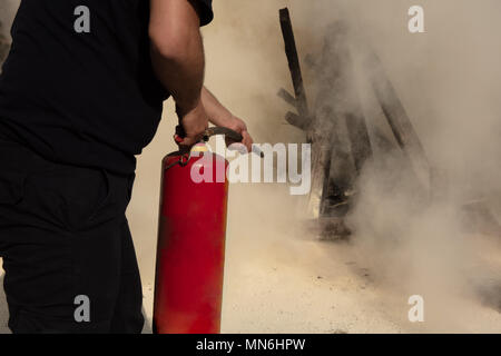 Young man pointing a powder type fire extinguisher forwards towards the fire in a serious situation Stock Photo