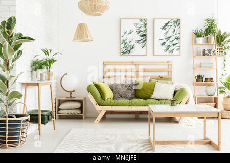 Globe shaped lamp placed on wooden table standing next to green couch in stylish living room interior Stock Photo