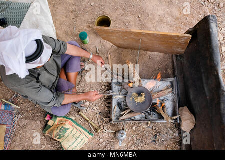 High angle view from a bedouin sitting on the ground and roasting beans on a fire to prepare traditional bedouin coffee Stock Photo