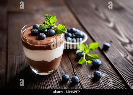 Layered chocolate and vanilla mascarpone dessert topped with blueberry, served in a glass jar Stock Photo