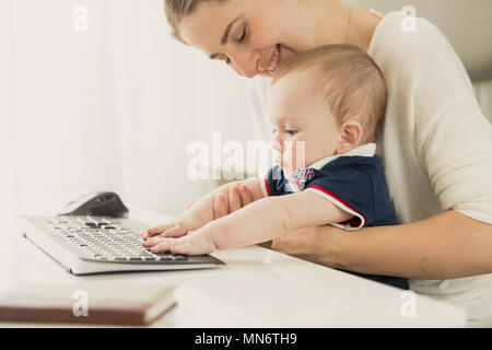 Toned portrait of smiling young mother teaching her baby son using computer at home office Stock Photo