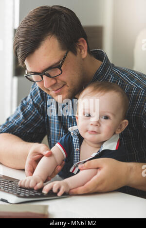 Toned portrait of smiling young father teaching his baby son using computer at office Stock Photo