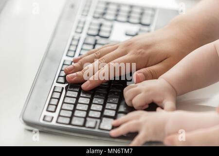 Closeup image of baby's and adult's hands on computer keyboard Stock Photo