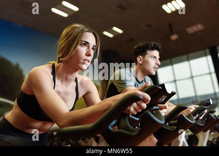 Attractive woman and man biking in the gym, exercising legs doing cardio workout cycling bikes. Couple in a spinning class wearing sportswear. Stock Photo
