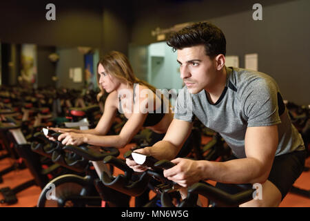 Attractive woman and man biking in the gym, exercising legs doing cardio workout cycling bikes. Couple in a spinning class wearing sportswear. Stock Photo