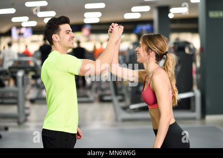 Smiling young man and woman doing high five in gym. Couple wearing sportswear Stock Photo
