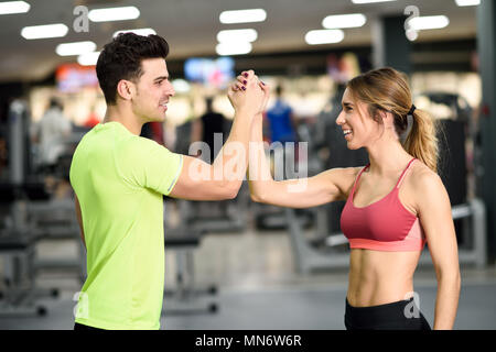 Smiling young man and woman doing high five in gym. Couple wearing sportswear Stock Photo