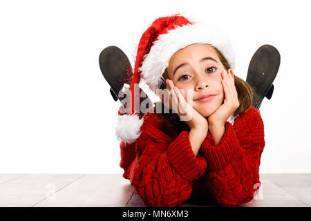 Adorable little girl wearing Santa hat laying on wooden floor on white background. Winter clothes Stock Photo