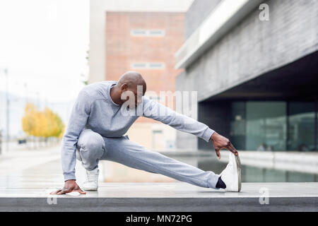 Black man doing stretching before running in urban background. Young male exercising Stock Photo