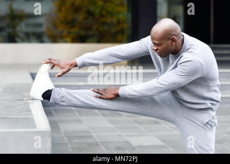 Black man doing stretching before running in urban background. Young male exercising Stock Photo