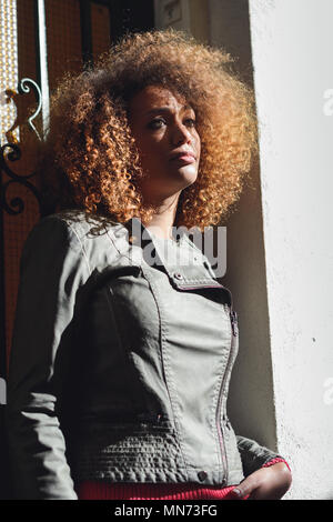 Beautiful young African American woman with afro hairstyle and green eyes wearing modern leather jacket in urban background. Stock Photo