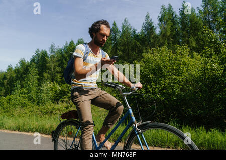 young man rides a bike and is looking at his smartphone Stock Photo