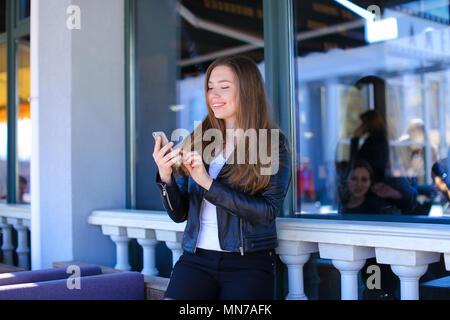 Pretty female person chatting by smartphone at street cafe. Stock Photo