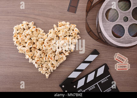 Equipment and elements of cinema on wooden table with popcorn heart. Concept of watching movies. Vertical composition. Top view. Stock Photo