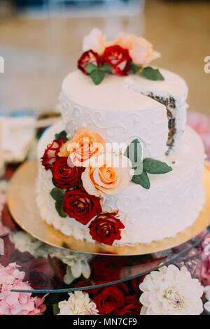 Vertical view of the white wedding cake decorated with red and orange roses. Stock Photo