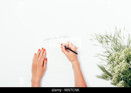 Woman making notes on blank paper page near bouquet of wild summer flowers, top view. Flat lay festive composition female hand with red manicure write Stock Photo