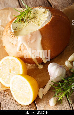 Baked Camembert with garlic and rosemary in a loaf of bread close-up on a table. vertical Stock Photo