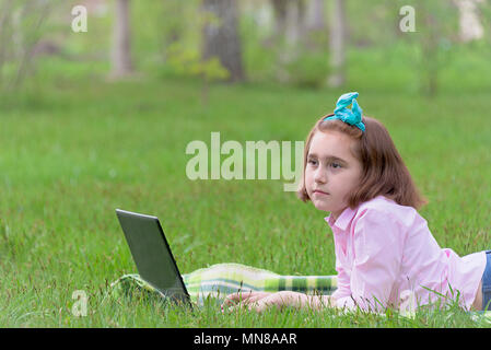 girl child with laptop outdoors resting on green grass Stock Photo