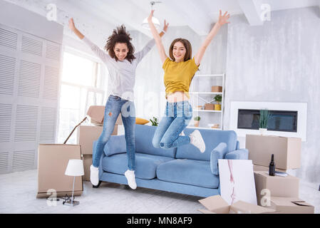 Cheerful young girls jumping happily in new apartment Stock Photo