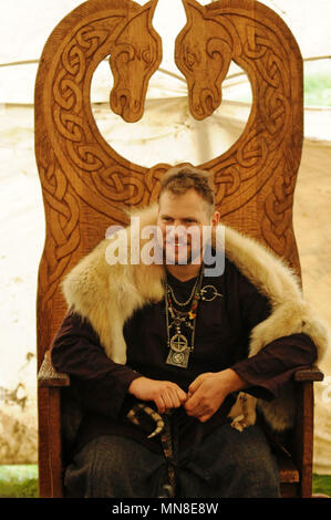 Viking sat in ornate wooden chair wearing animal skin Stock Photo