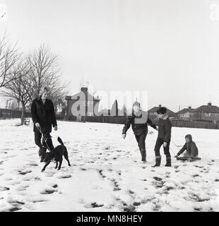 1965, January, wintertime and a mother, her three sons and the family dog enjoy the snow in the local park outside, England, UK. Stock Photo