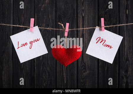 Paper stickers with text Love you Mom & red heart hanging on rope on gray wooden background. Happy Mother's Day concept. Stock Photo